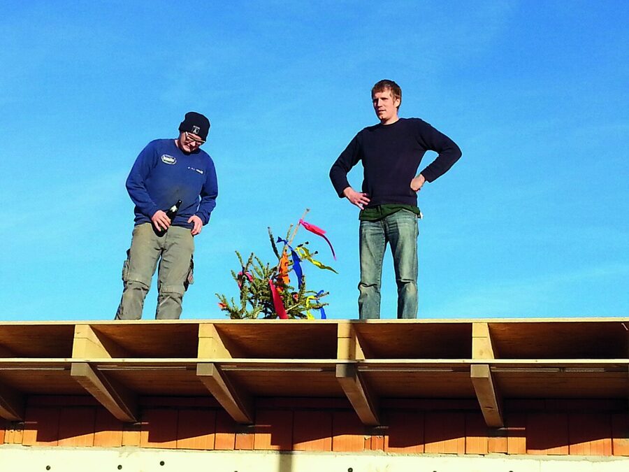 Zwei Männer stehen mit dem geschmückten Firstbaum auf dem Rohbau